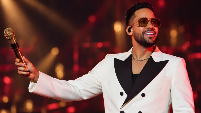 Romeo Santos con traje blanco y micrófono dorado durante una presentación.